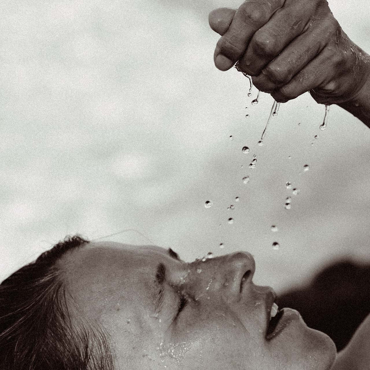 Water droplets falling from a hand onto an upturned face, eyes closed