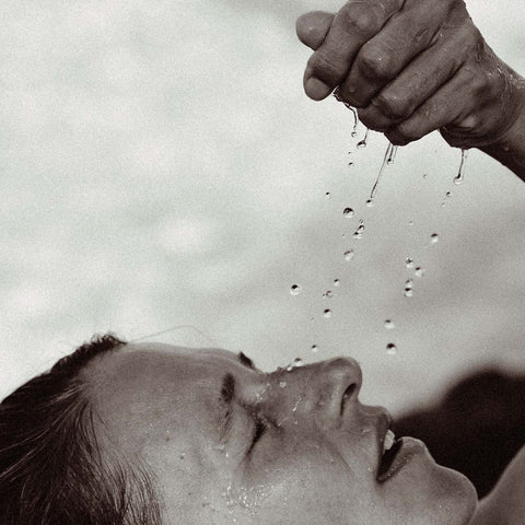 Water droplets falling from a hand onto an upturned face, eyes closed